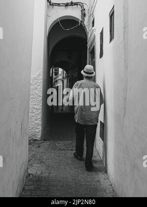 A vertical shot of a man visting the Old Medina at Tanger in Morocco in grayscale Stock Photo