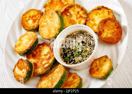 pan fried zucchini in egg batter served with soy dipping sauce on plate on white wooden table, Hobak Jeon, korean cuisine Stock Photo