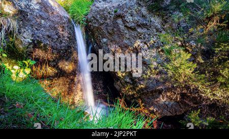 Small waterfall between rocks in the mountain with green plants and long exposure. Stock Photo