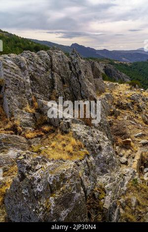 Landscape of rocks with green plants, dramatic sky with clouds and distant mountains. Stock Photo