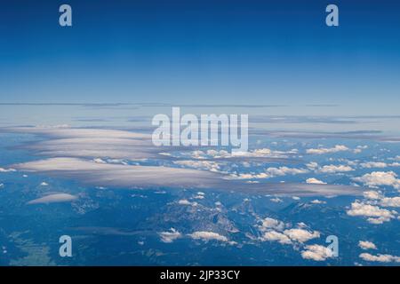 Sky with cumulus and cirrus clouds and mountains below, aerial view. Stock Photo