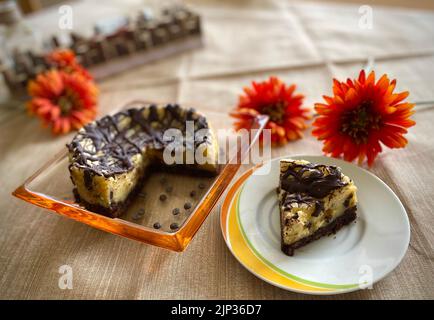 A closeup of a delicious vegan chocolate chip cheesecake served on a table with orange gerberas Stock Photo