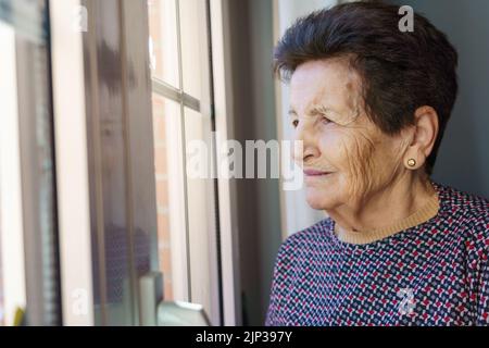 White 90 year old senior woman looking out the window thoughtfully. Stock Photo