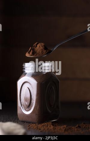 ground coffee in a metal spoon on top of glass jar, against on a dark textured background, soft-focus background with copy space Stock Photo