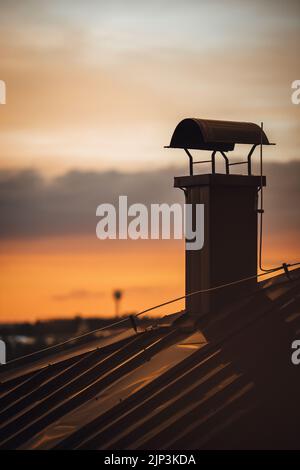 A vertical shot of house chimney against blur sunset sky background Stock Photo