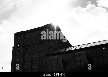 A grayscale of the sun shining behind an old stone building in Dublin, Ireland Stock Photo