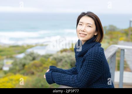 Portrait of happy asian woman wearing jumper and leaning on balcony alone Stock Photo