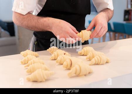 Hands of a baker man cooking small croissants at home, finishing rolling the puff pastry Stock Photo