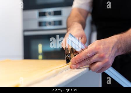 A man measuring puff pastry and making cuts for cooking homemade croissants, work in the kitchen at home Stock Photo