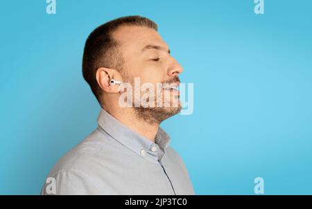 Profile Portrait Of Man Listening Music Wearing Earbuds, Blue Background Stock Photo