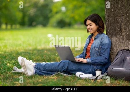 E-learning Concept. Arab Female Student With Laptop Sitting Under Tree In Park Stock Photo