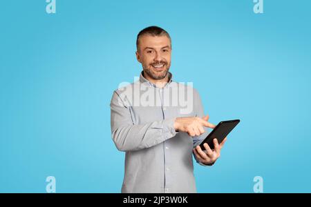 Happy Mature Male Using Digital Tablet Browsing Intetrnet, Blue Background Stock Photo