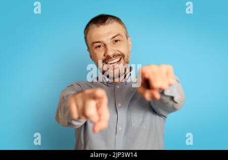 Cheerful Middle Aged Man Pointing Fingers At Camera, Blue Background Stock Photo