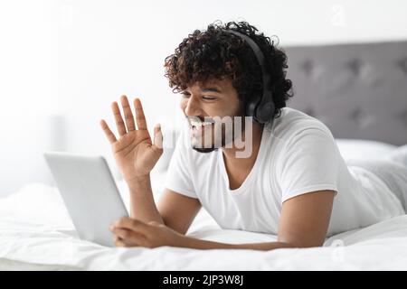 Handsome indian guy lying on bed, having video conference Stock Photo