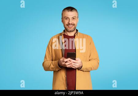 Cheerful Middle Aged Male Holding Smartphone Over Blue Background Stock Photo