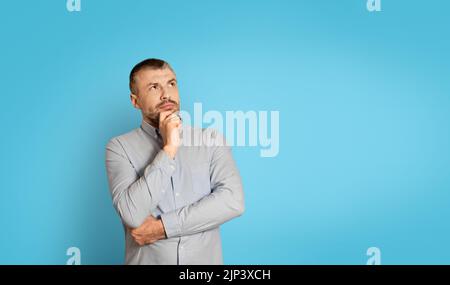 Thoughtful Middle Aged Man Thinking Touching Chin On Blue Background Stock Photo