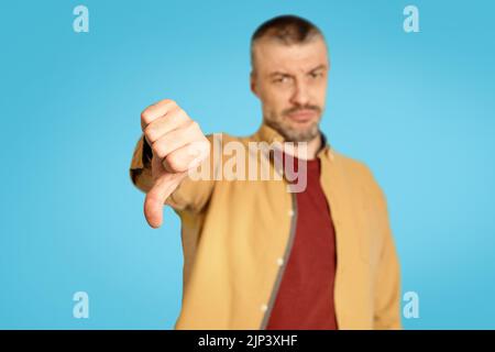 Discontented Mature Male Gesturing Thumbs Down Disapproving Offer, Blue Background Stock Photo