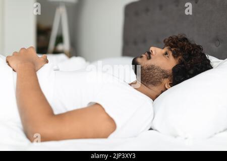 Closeup of depressed eastern guy lying in bed alone Stock Photo