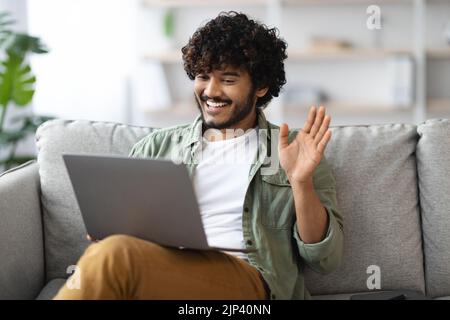 Positive eastern guy having video call, using computer at home Stock Photo
