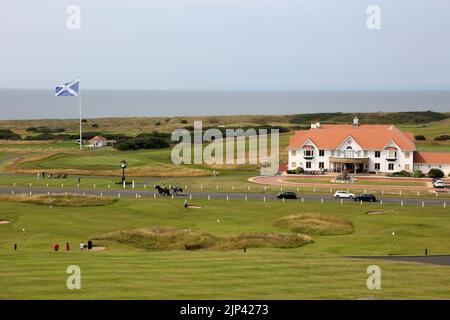 Trump Turnberry, Ayrshire, Scotland  UK..One of the largest saltire flags in Scotland  dominates the area and can be seen from miles around. This view seen from the Turnberry hotel with the starters hut for the first tee, practice greens and the 18th green. Also in the photo is the iconic large clock which bear Donald Trump's name. Golfers practice on the greens, with some teeing of from the 1st tee. Horse riders pass by On the horizon is the Firth of Clyde on the West Coast of Scotland. To the right of the picture is the Club house Stock Photo