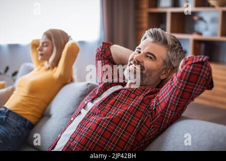 Cheerful middle aged handsome european man and woman enjoy rest and relaxation, dreaming on sofa Stock Photo