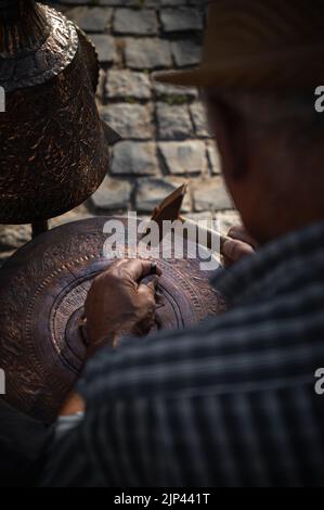 A vertical shot from behind a male copper artist during the work process on a street Stock Photo