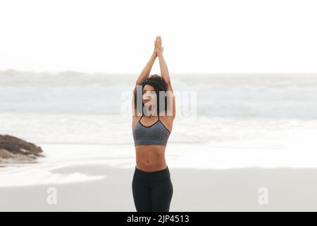 Fit woman standing with raised arms on a beach against an ocean at sunset Stock Photo
