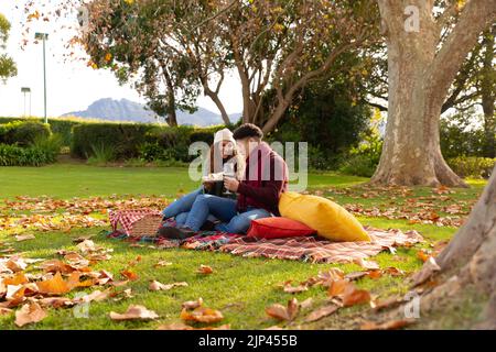 Image of happy diverse couple having picnic in autumn park Stock Photo