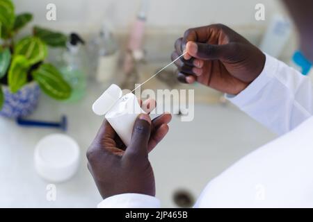 Over shoulder view of african american man using dental floss in bathroom Stock Photo
