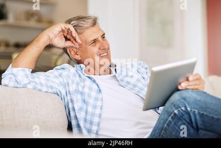 Relaxed, happy and carefree man relaxing on couch calm, smiling, happy and joyful while holding his tablet in his hands. Casual male enjoying his Stock Photo