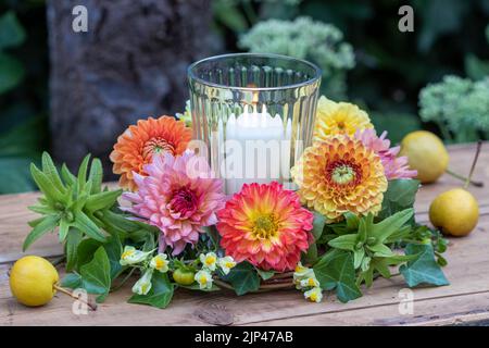 arrangement with wreath of dahlias, true toadflax and ivy and candle in glass Stock Photo
