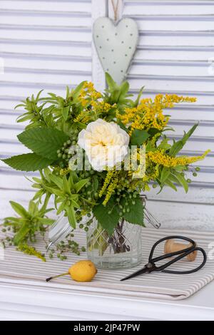 bouquet of white rose, hazelnut tree fruits, goldenrod and elder berries in glass Stock Photo