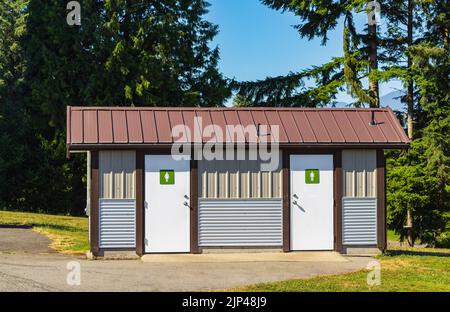 Public toilet in park at sunny summer day. Wooden restroom or toilet building in remote forest in British Columbia. Bathrooms or WC. Public automatic Stock Photo