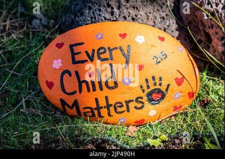 A handpainted rock that says 'Every Child Matters' on the ground against a tree at the Kamloops Residential School.  Unmarked remains have been found Stock Photo