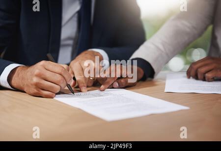 Please sign here if you agree with the terms. Closeup shot of two unrecognizable businesspeople going through paperwork in an office. Stock Photo
