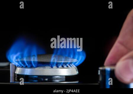 Gas stove on a black background. Fragment of a gas kitchen stove with a blue flame, close-up. Energy crisis concept, rise in price or price of gas. Stock Photo