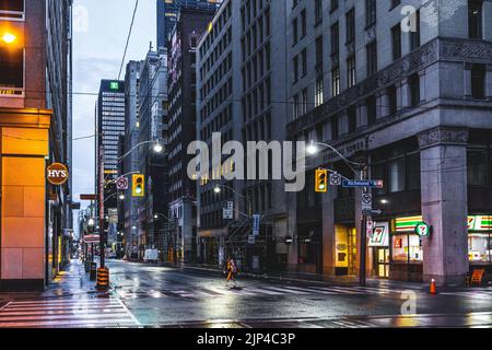 A beautiful sunrise in Downtown Toronto with a woman crossing the road illuminated by street lights Stock Photo