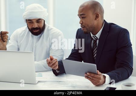 Get collaborative, get productive. two businessmen using a digital tablet and laptop while having a discussion in a modern office. Stock Photo
