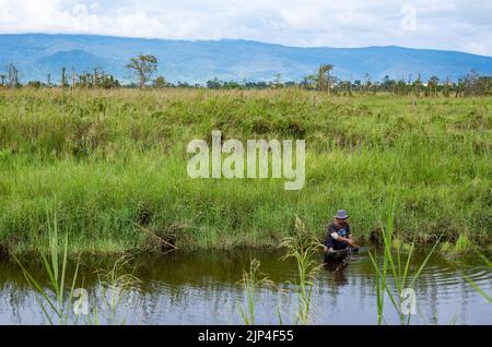 A local man in a dugout canoe fishing in a lake. Sulawesi, Indonesia. Stock Photo