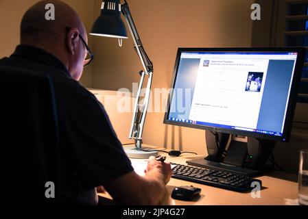 An adult man wearing glasses working from home in front of a computer Stock Photo