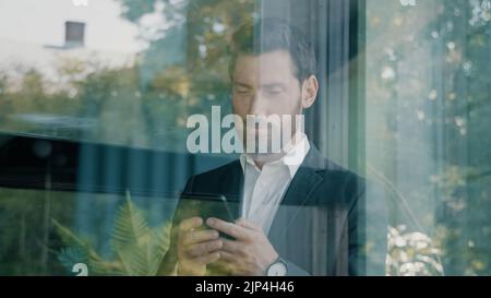 Bearded 40s adult mature Caucasian businessman looking phone man typing text email online mobile app using smartphone browsing searching in Internet Stock Photo