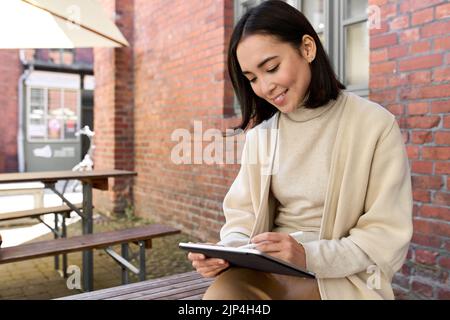 Happy professional Asian woman using digital tablet pad sitting outside. Stock Photo