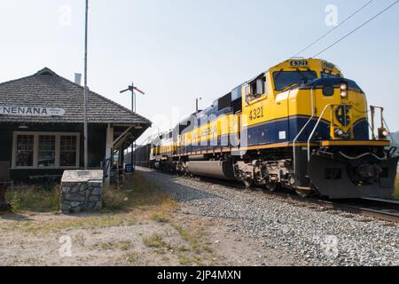 A train engineer waves out the window as his Alaska Railroad train engine passes the railroad station in Nenana, Alaska, USA Stock Photo