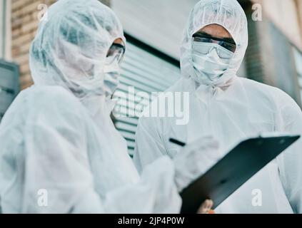 Healthcare workers wearing protective hazmat suits writing a medical report about covid cases or statistics. First responders filling in a form after Stock Photo