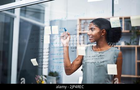 Female leadership and marketing professional brainstorming innovation ideas, writing on transparent board with sticky notes in office. Young Stock Photo