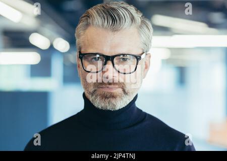 Close-up photo portrait of successful serious and mature businessman, investor in glasses looking thoughtfully at camera, man at work inside office Stock Photo