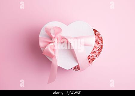 Festive heart shaped white gift box isolated on pastel pink background. Women's day, Valentine's day greeting card. Stock Photo