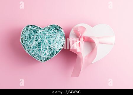 Festive heart shaped open gift box with shred paper on pastel pink background. Present concept. Stock Photo