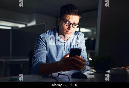 Confused businessman texting on his phone at the office at night. Handsome, confident and corporate caucasian male looking at messages from coworkers Stock Photo