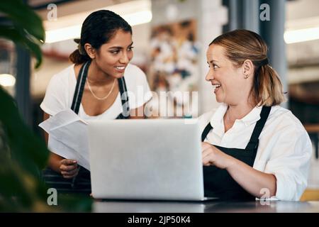 Small business owner working on a budget strategy or ordering stock online with an employee using a laptop in her store. Female entrepreneur talking Stock Photo